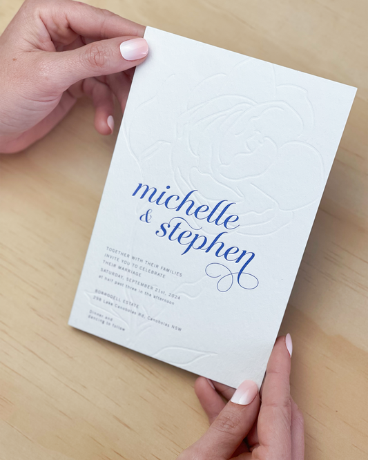 Hand holding our Aurora Rose wedding invitation featuring blind deboss rose motif. Designed by Communique Design