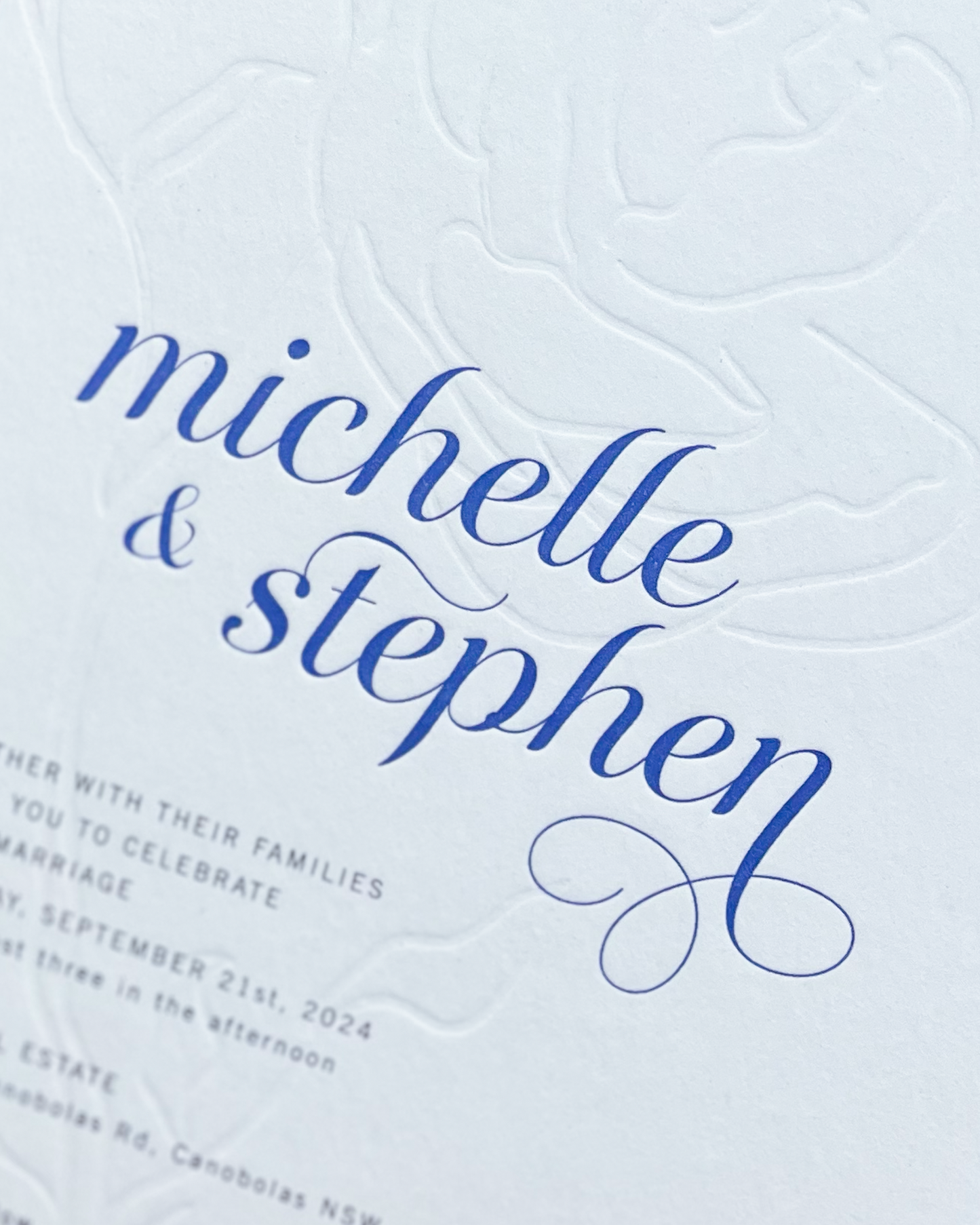 Close up of the Aurora Rose wedding invitation showing blind deboss rose motif and names. A design by Communique Design.