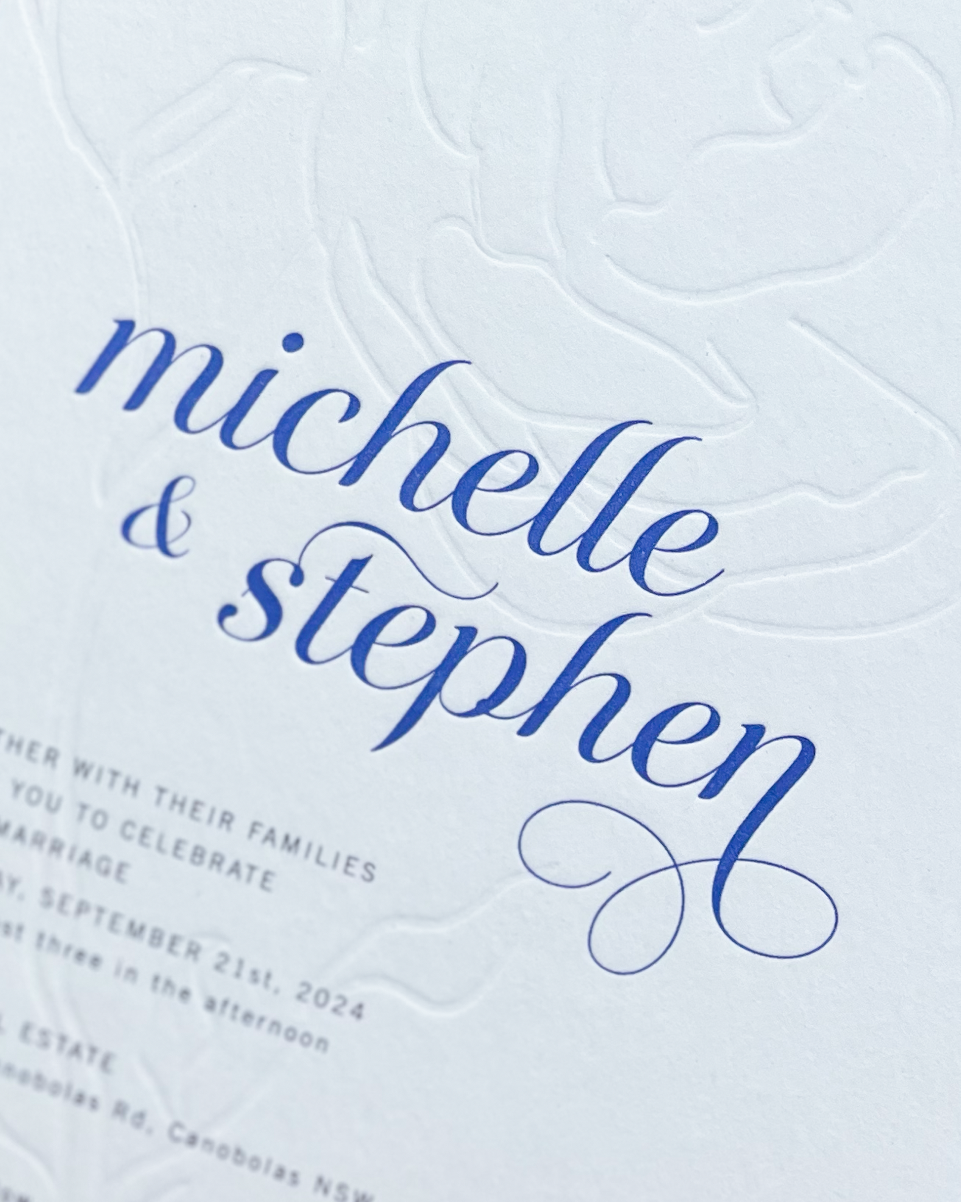 Close up of the Aurora Rose wedding invitation showing blind deboss rose motif and names. A design by Communique Design.
