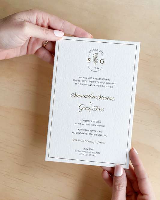 Hand holding a the classic Sorrento wedding invitation with gold foil a highlight. A design by Communique Design.