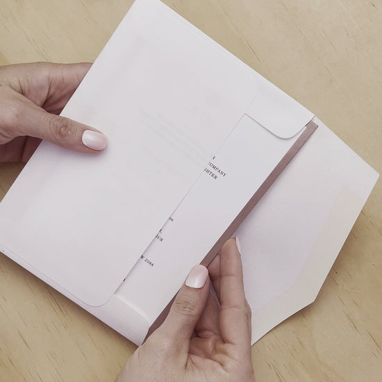 Duet wedding invitation shown being revealed from the envelop. Rose foil is a highlight of this invitation. A design by Communique Design.